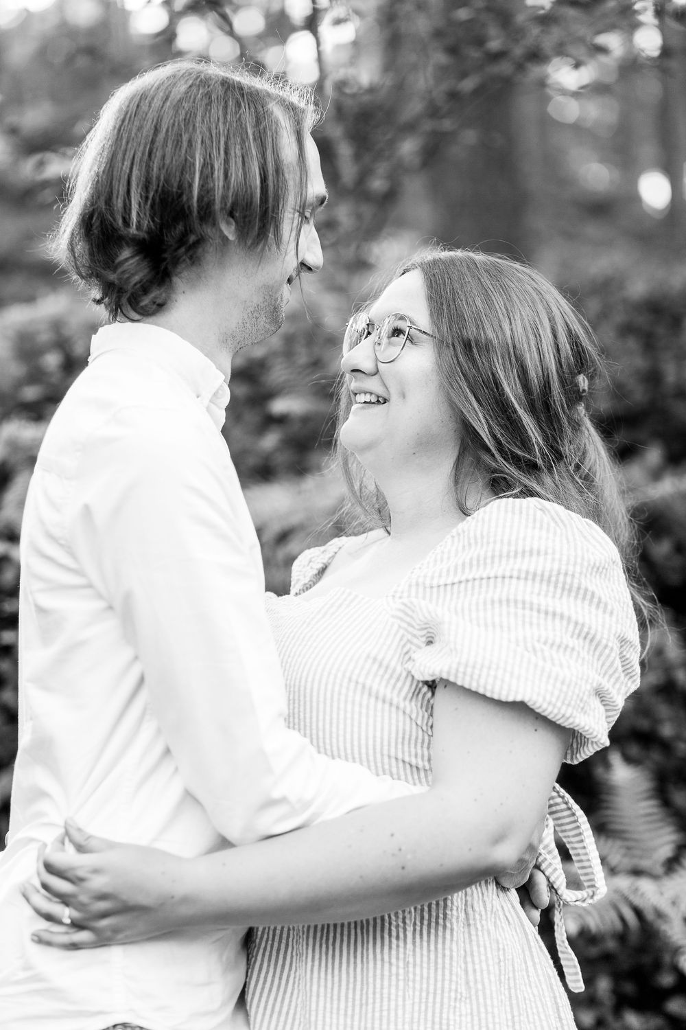 A romantic black and white portrait of a couple embracing and gazing at each other in an outdoor setting.