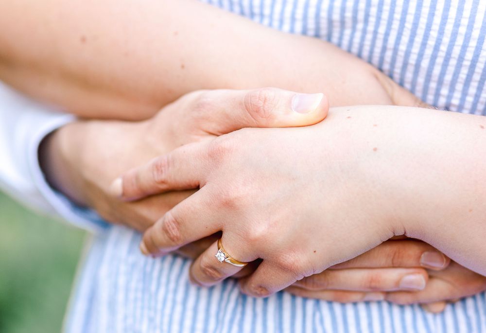 Close-up of two hands clasped together in a loving embrace against a blue and white striped background.