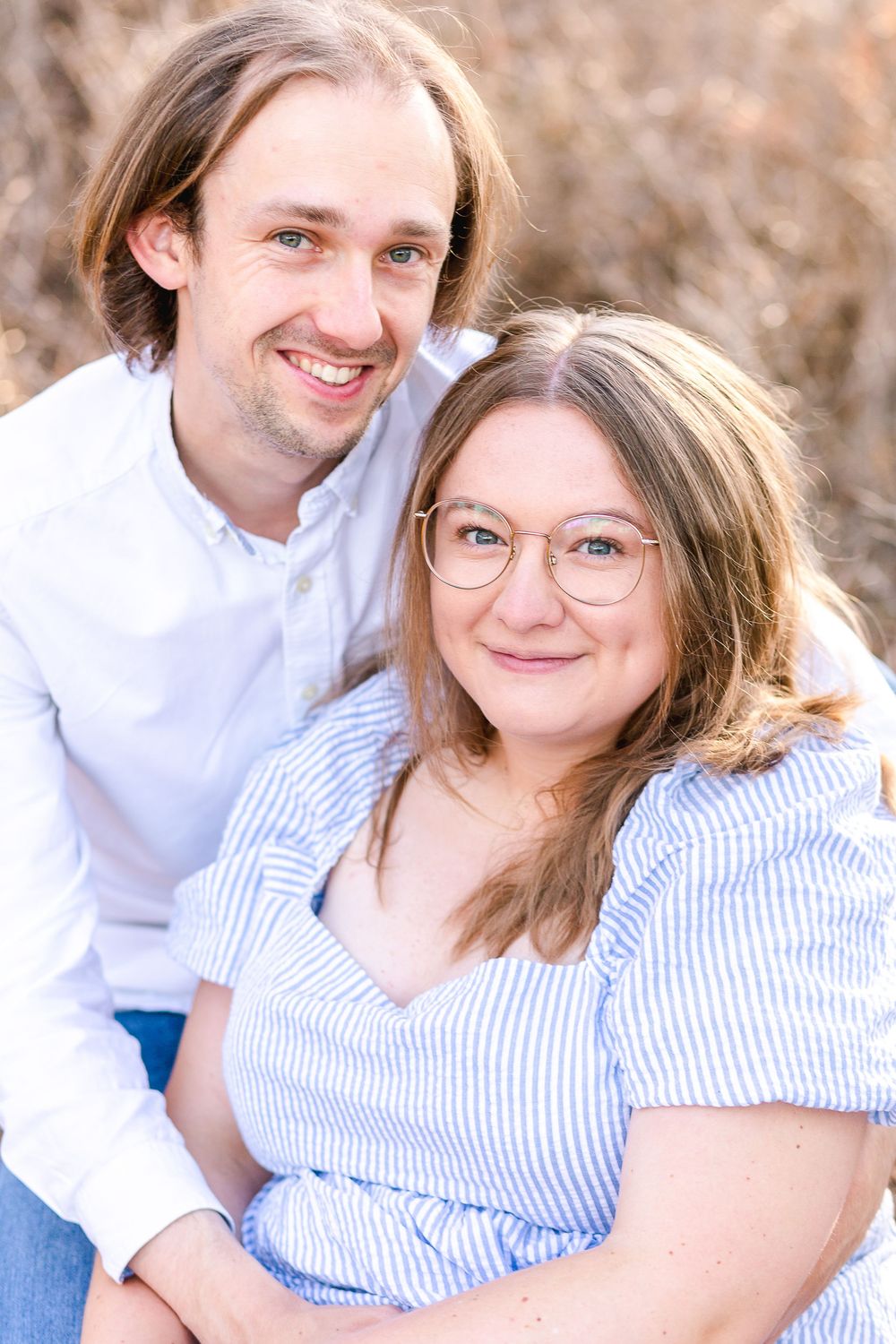 A couple in white and blue striped clothing pose together outdoors in a series of candid romantic photos.