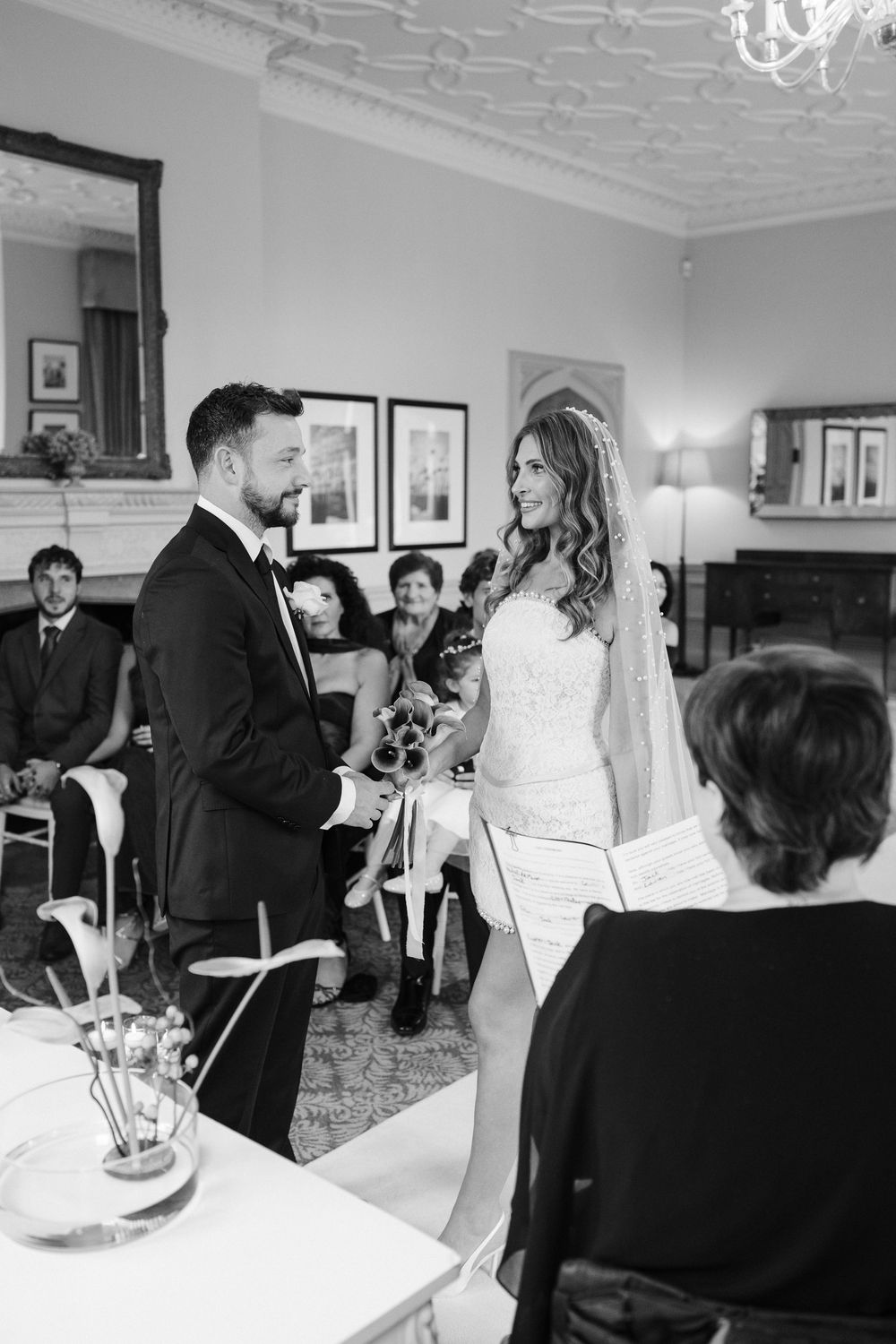Wedding guests gather in an elegant room with ornate molding and black and white decor for a reception celebration.