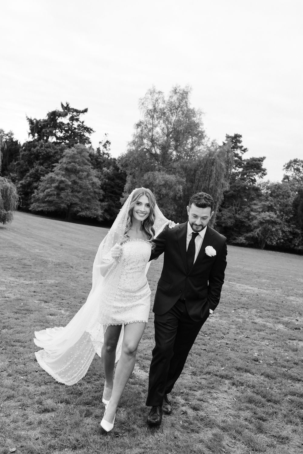 A couple in wedding attire playfully runs and poses together in a grassy field on their special day.