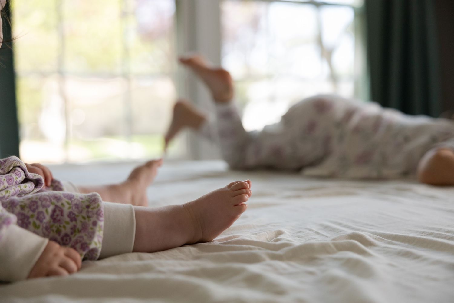 Sioux City, Iowa photographer. Close-up of two young children lying on white bed with bare feet visible in soft natural light.