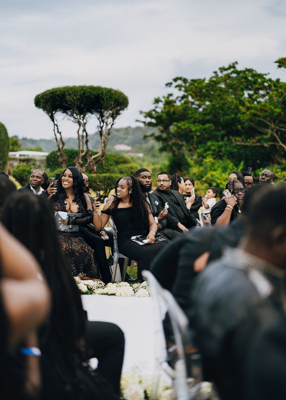 A large crowd of people celebrating outdoors at what appears to be a graduation ceremony with trees in the background.