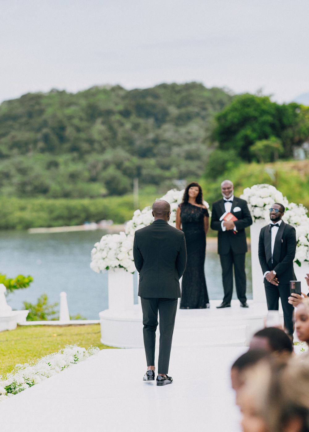 Wedding ceremony setup with white floral arrangements along the aisle by a serene lakeside venue.