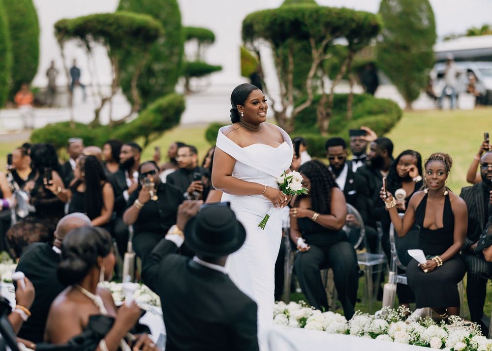 Wedding guests in black attire surround and celebrate with someone in a white dress at an outdoor celebration.