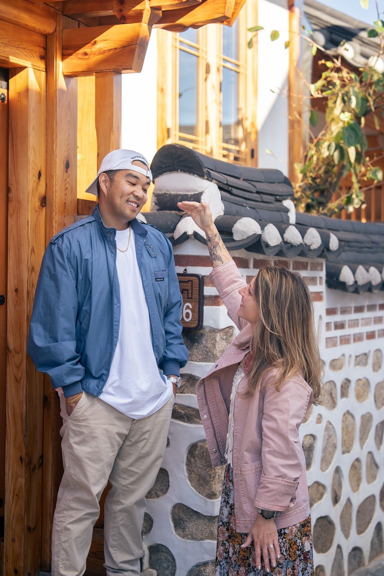 Couple in casual attire sharing a candid moment against a rustic wood and stone wall backdrop.
