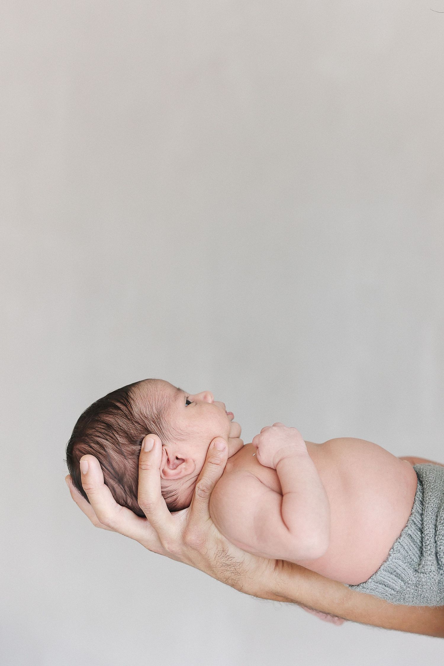 A parent's hand gently supports a sleeping newborn baby's head against a light gray background.