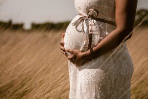 Detail van een zwangere vrouw in een kanten jurk die liefdevol haar buik omarmt, een warm en stijlvol zwangerschapsportret in Antwerpen.