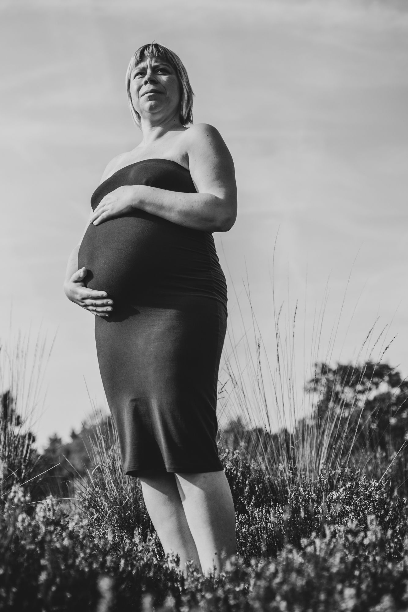 Zwartwit zwangerschapsportret van een vrouw die trots poseert op de heide, een krachtig en natuurlijk beeld uit de provincie Antwerpen.