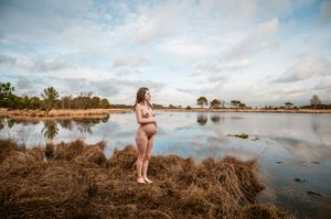 Artistieke en serene zwangerschapsfoto in de natuur met weids uitzicht en zachte lichtreflecties in Antwerpen.