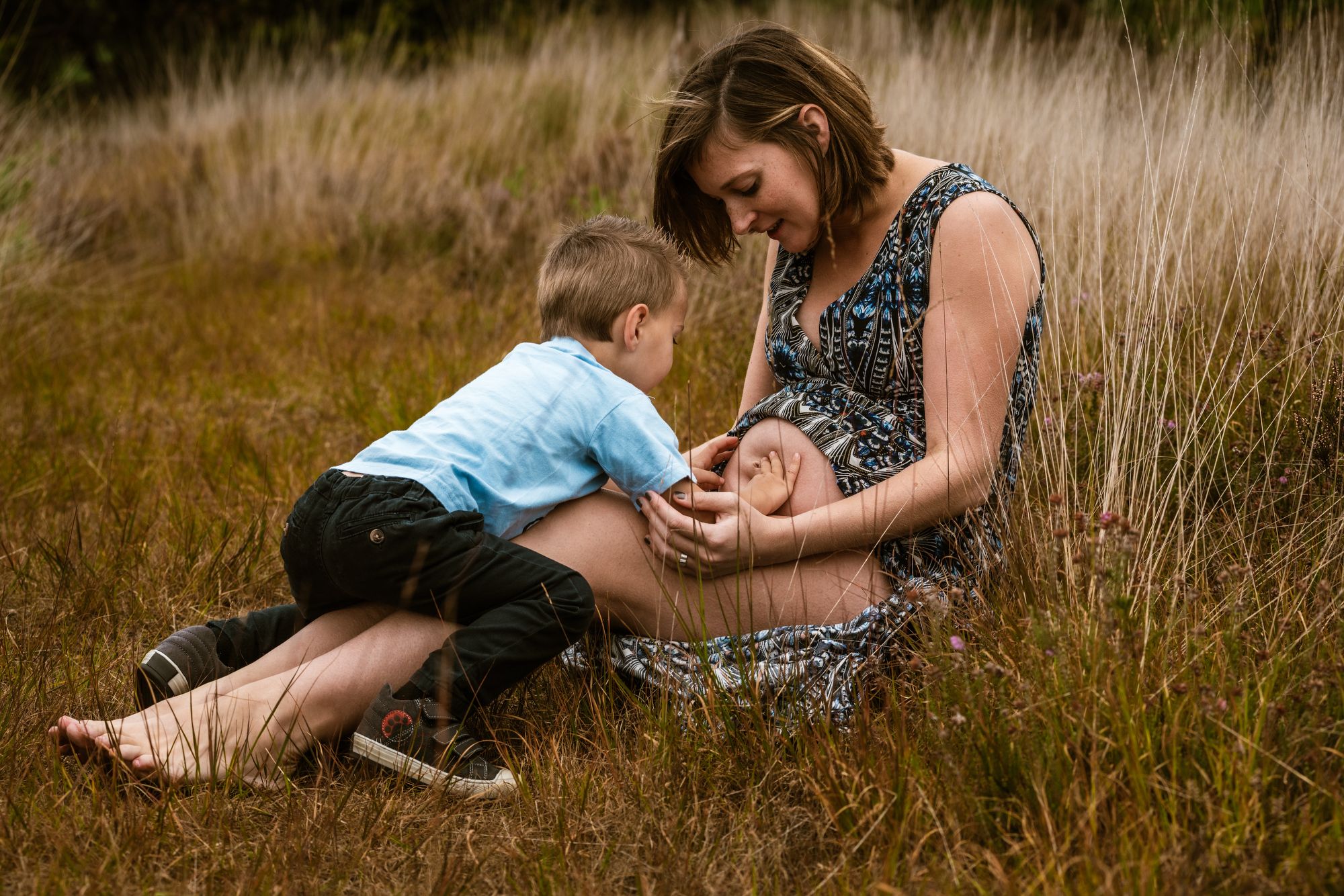 Mama en zoontje delen een teder moment terwijl hij de zwangere buik aanraakt tijdens een natuurlijke sessie in provincie Antwerpen.