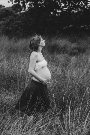 Zwangere vrouw in een rustig natuurgebied, staand in hoog gras tijdens een puur zwangerschapsmoment.