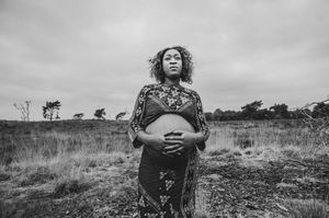 Zwartwit zwangerschapsportret van een vrouw in een traditionele jurk, een krachtig en sereen beeld uit de provincie Antwerpen.