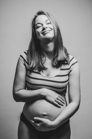 Zwartwit studioportret van een zwangere vrouw met een warme glimlach, een spontaan en stijlvol moment uit de provincie Antwerpen.