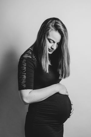 Zwartwit studioportret van een zwangere vrouw die zacht naar haar buik kijkt, een tijdloos beeld gemaakt in de provincie Antwerpen.