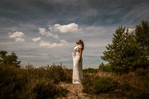 Zwangere vrouw in een elegante jurk staand in de natuur, een krachtig en rustig zwangerschapsportret in de provincie Antwerpen.