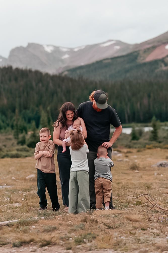 A group stands together in a field with majestic mountain peaks and evergreen forests creating a scenic backdrop.