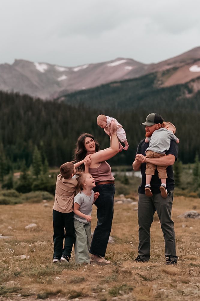 A group enjoying a playful moment together in a scenic mountain meadow with snow-capped peaks in the background.