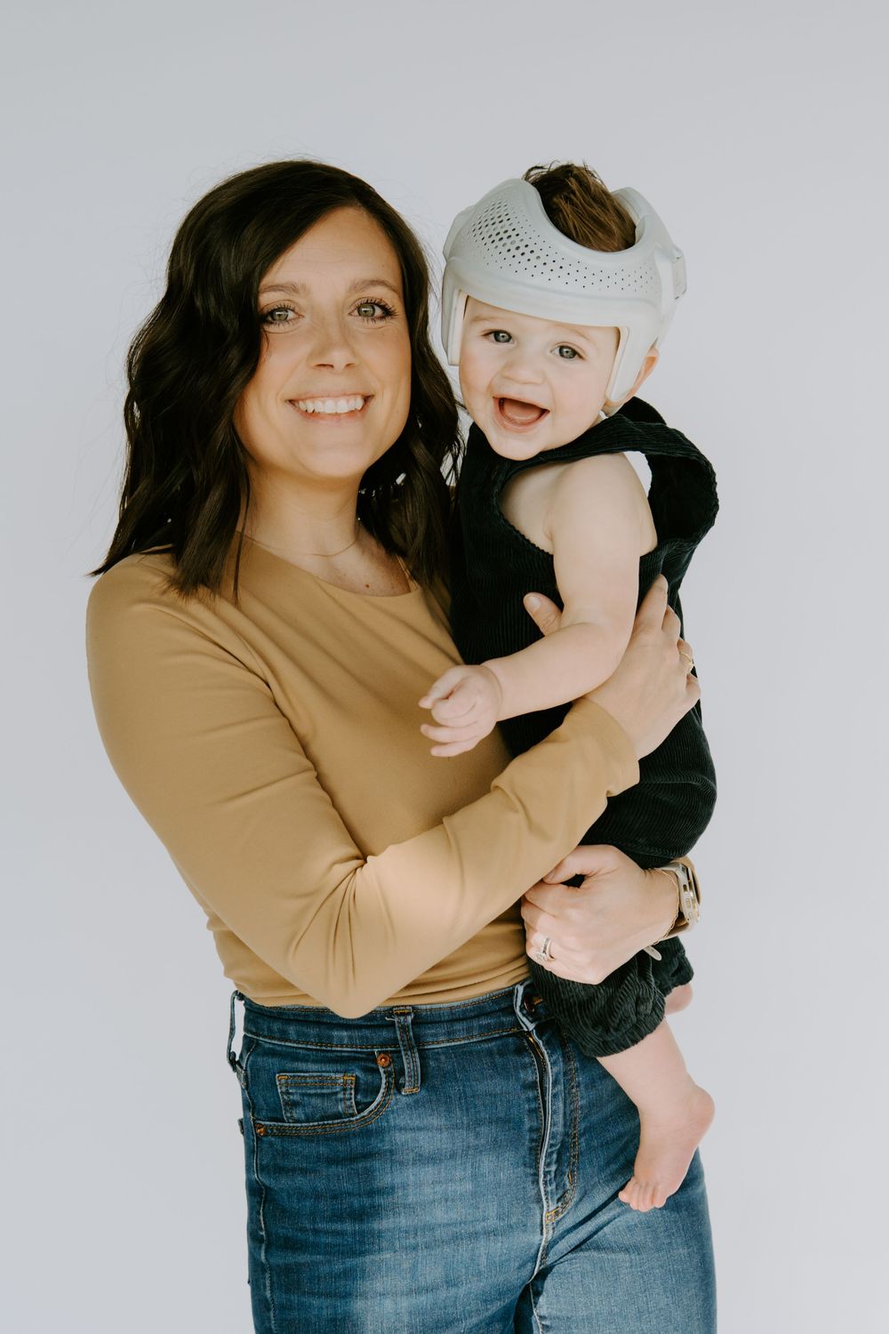 Mother and baby share playful moments against white studio backdrop.