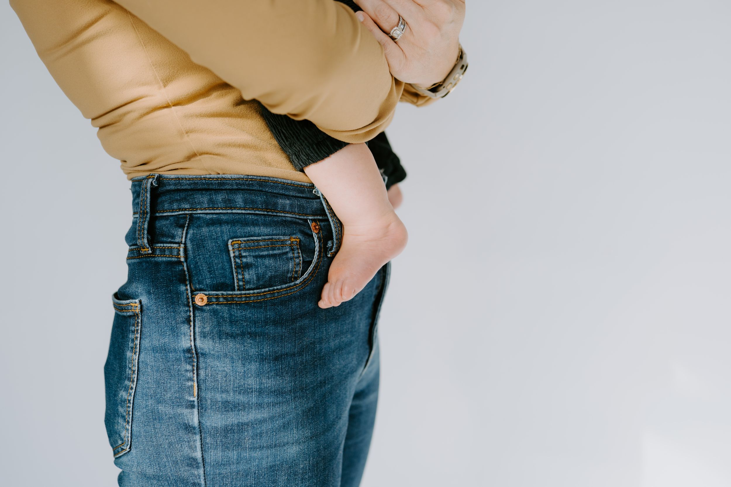 Woman in camel sweater and jeans poses against white studio background.