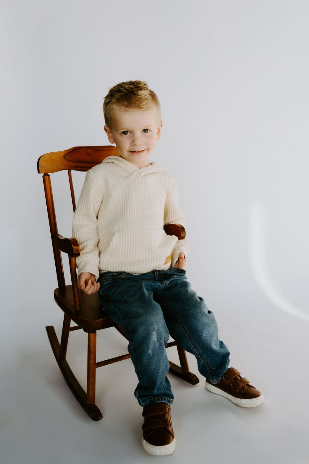 A series of candid shots showing a small child in a cream sweater and jeans sitting on a wooden rocking chair.