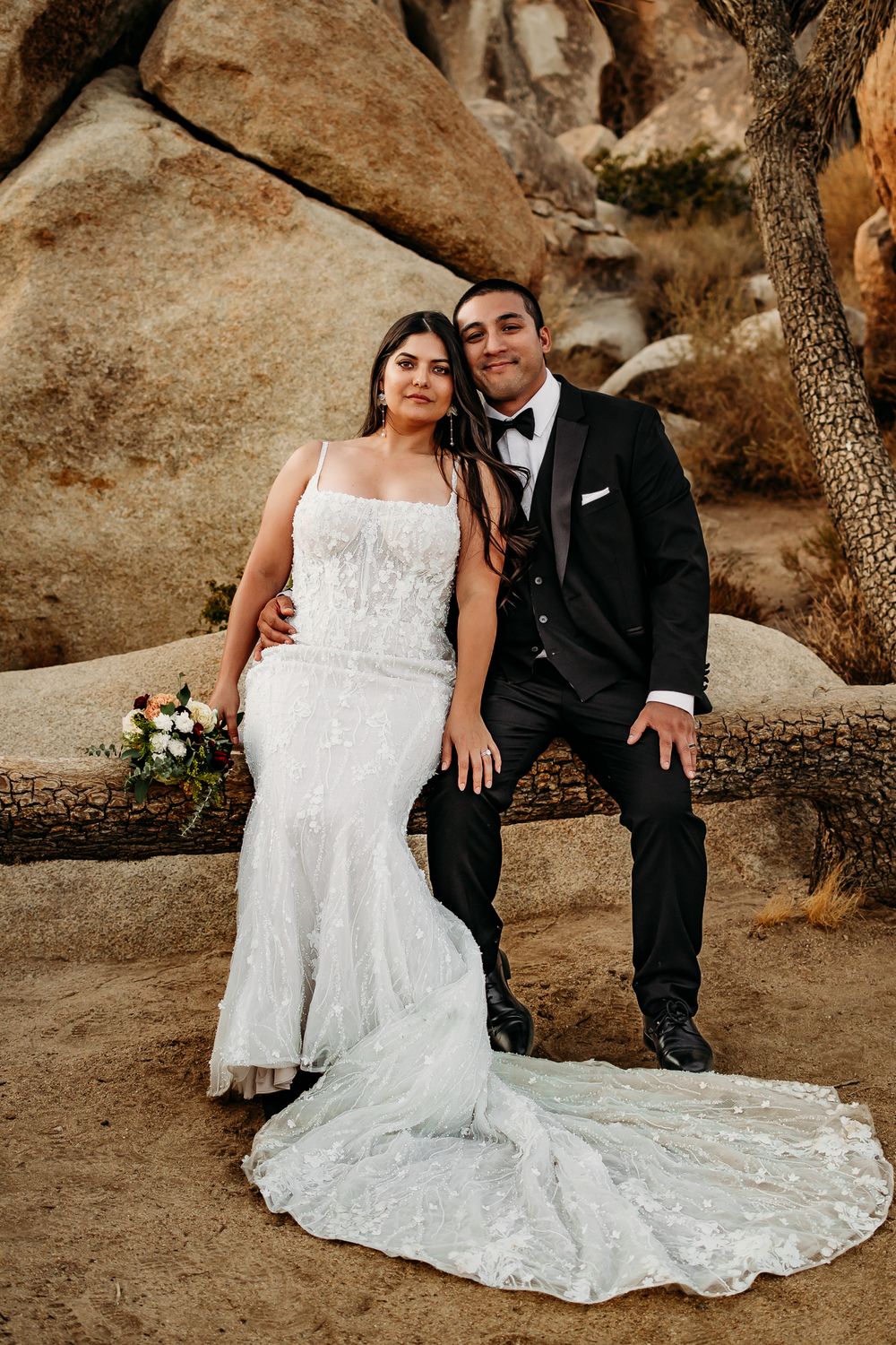 A wedding couple poses on natural stone steps in a desert landscape with Joshua trees.