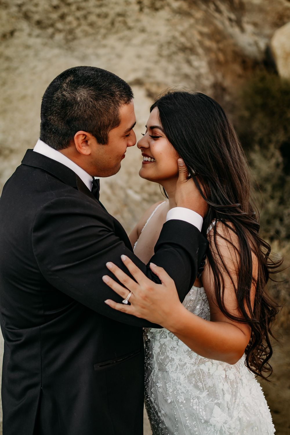 Romantic wedding couple shares intimate moment against rocky backdrop in black and white tones.