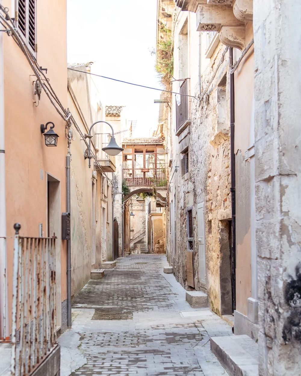 A narrow stone alleyway lined with aged buildings and soft warm light filtering through.
