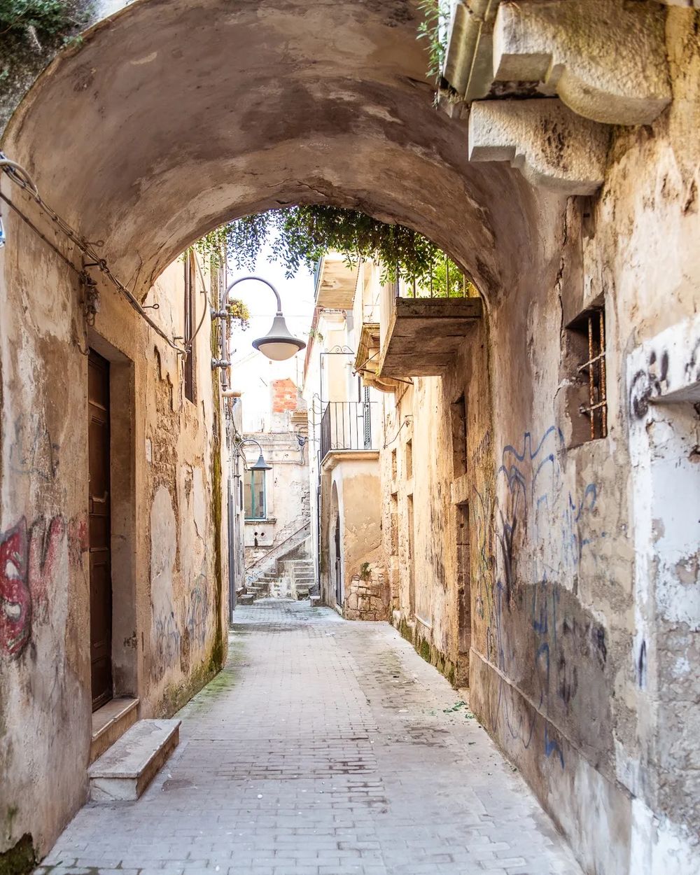 A narrow stone alleyway with an old archway leads through a quiet historic town.