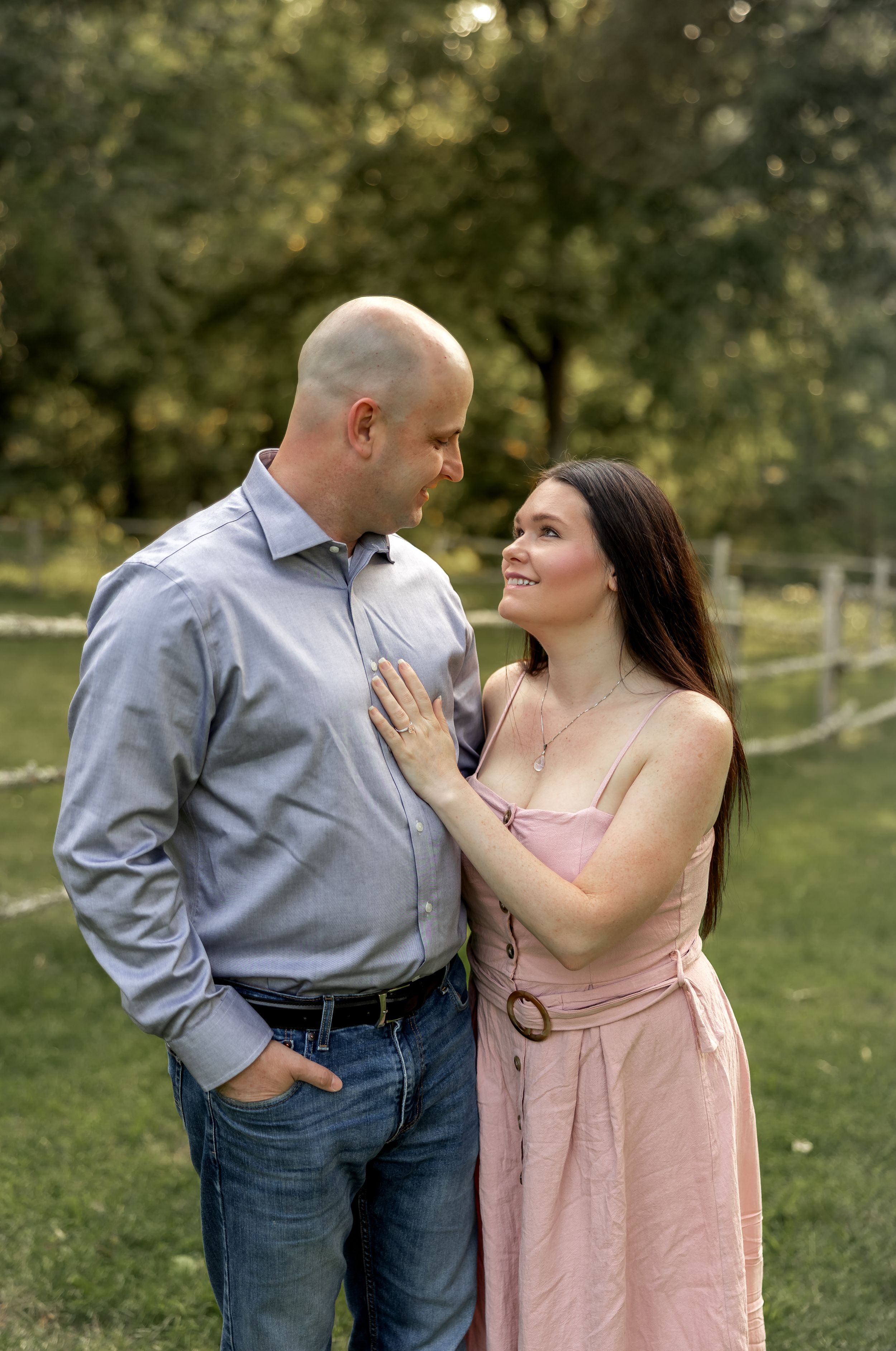 A couple shares a tender moment in a sunlit park wearing coordinated pink and grey outfits.