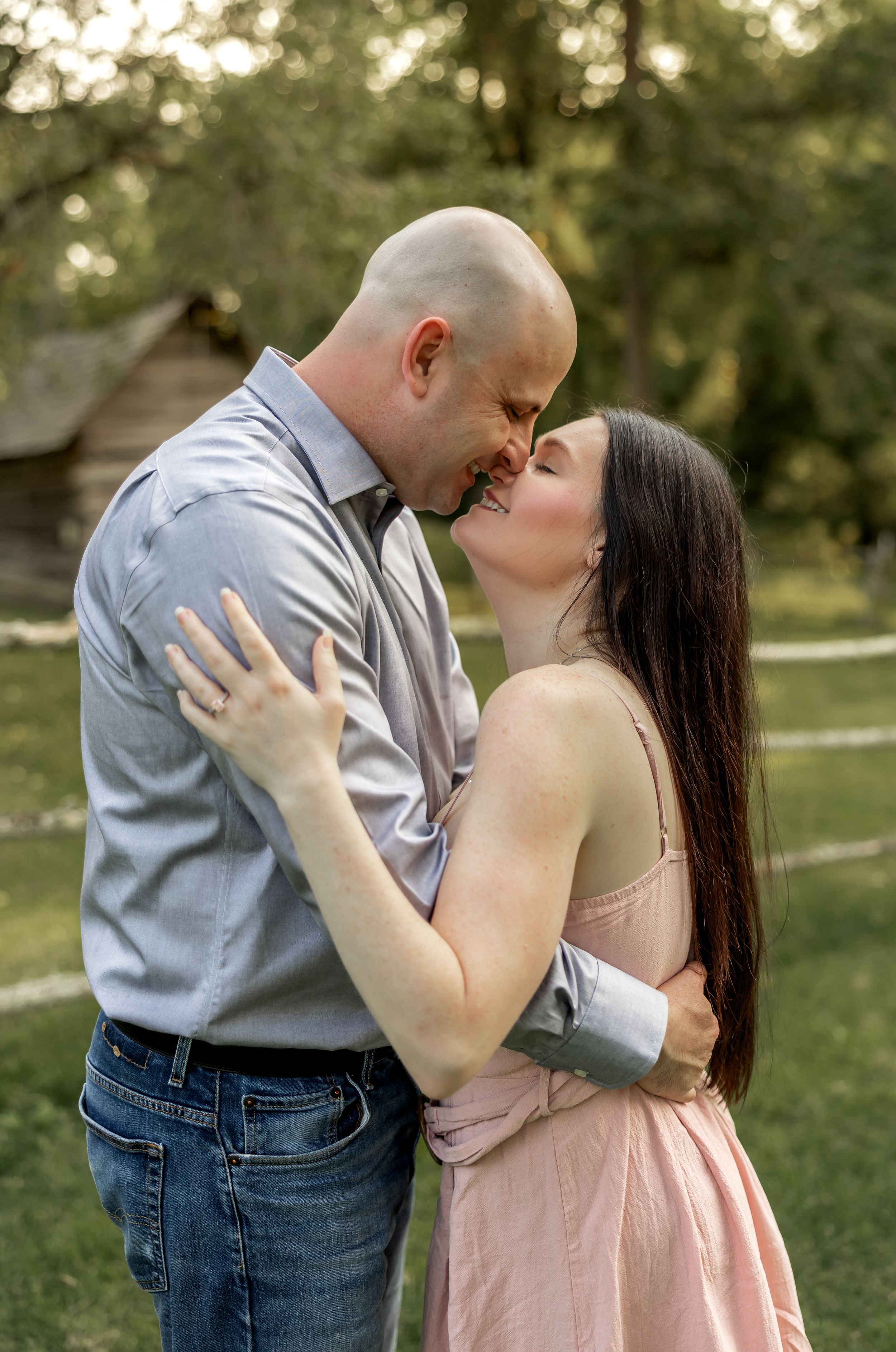 A romantic couple embraces in a park during golden hour while wearing casual attire.