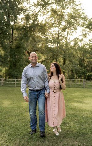 A couple walks hand in hand through a grassy park during a photo session.