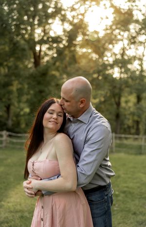 A romantic outdoor photoshoot at sunset with a couple embracing in a park setting.