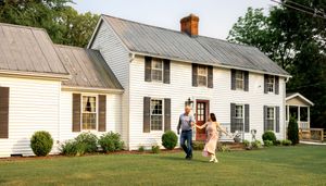 Long white farmhouse with metal roof and brown shutters photographed from the side.