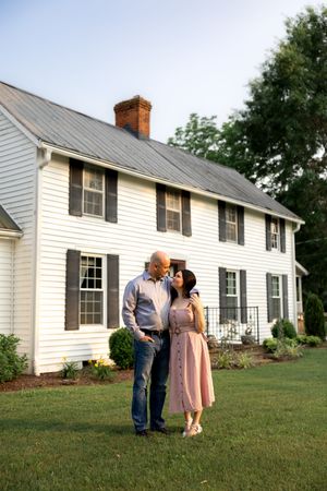 Couple shares an intimate moment on the lawn of a traditional white farmhouse.