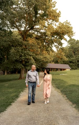 Couple walking hand in hand down a gravel path surrounded by trees at sunset.