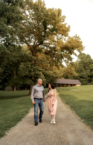 A couple walking hand in hand down a tree-lined path during golden hour.