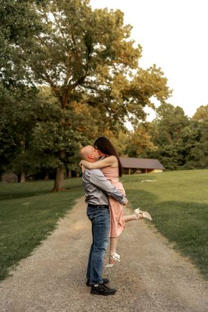 A playful couple sharing an intimate moment on a gravel path surrounded by trees.