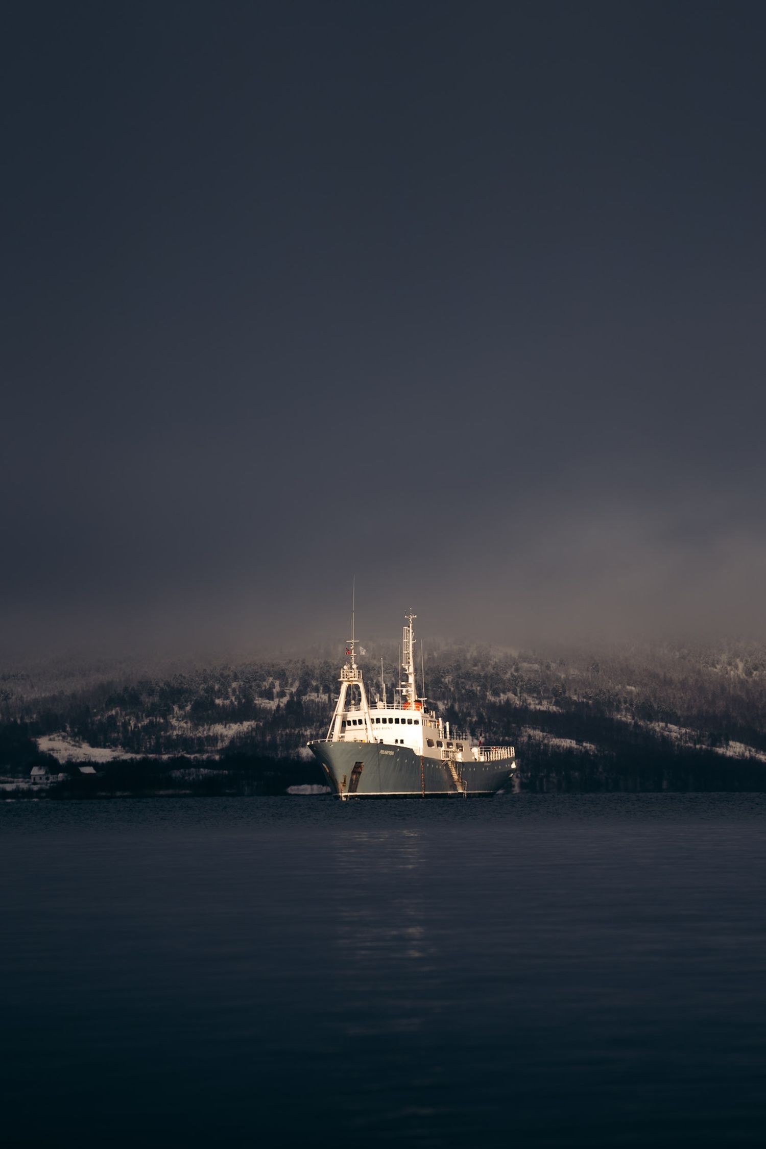 bateau polarfront naviguant sous un ciel sombre et un seul rayon de soleil qui l'illumine