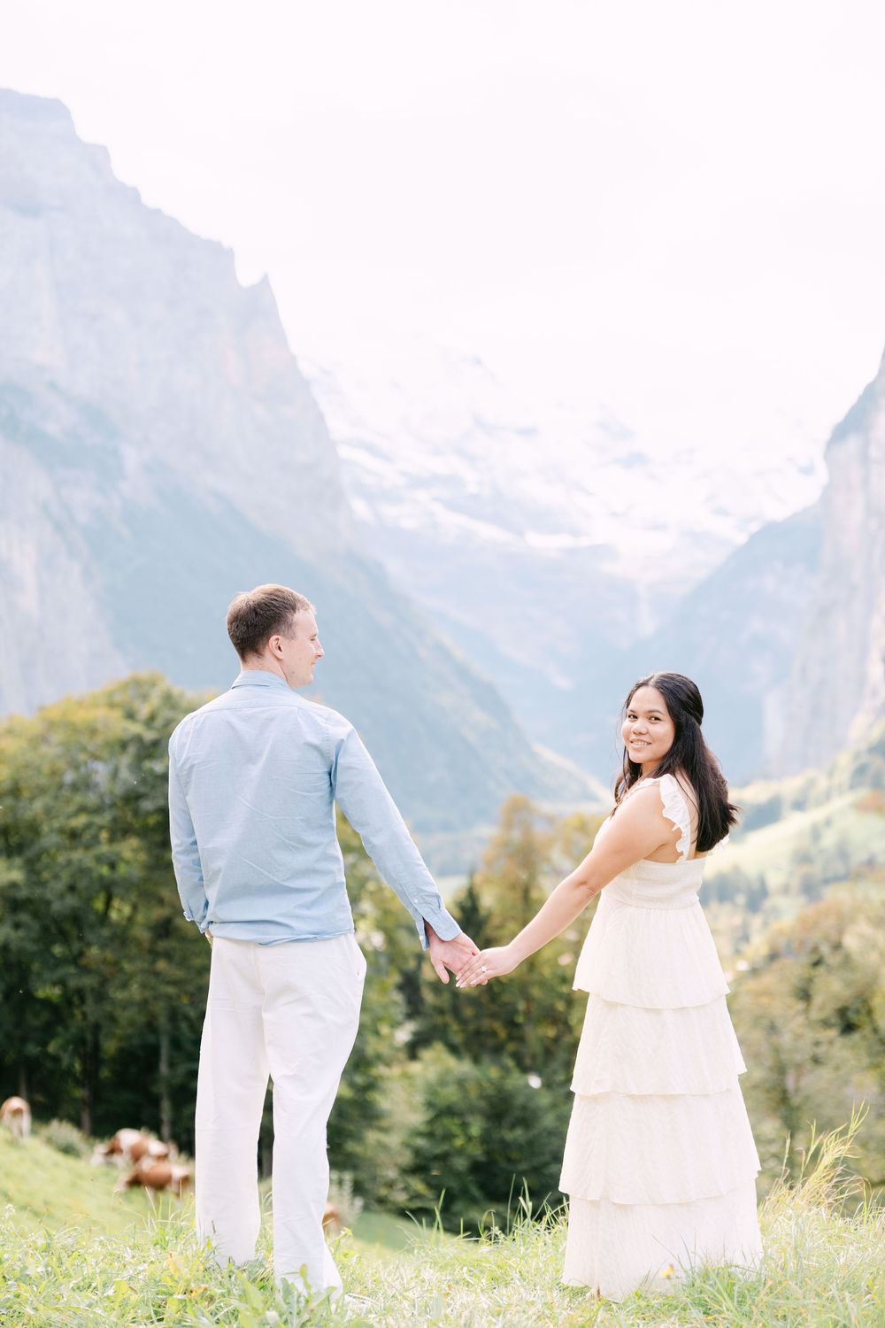 Couple in white and blue outfits share a romantic moment in a scenic mountain meadow with alpine peaks in background in Lauterbrunnen.