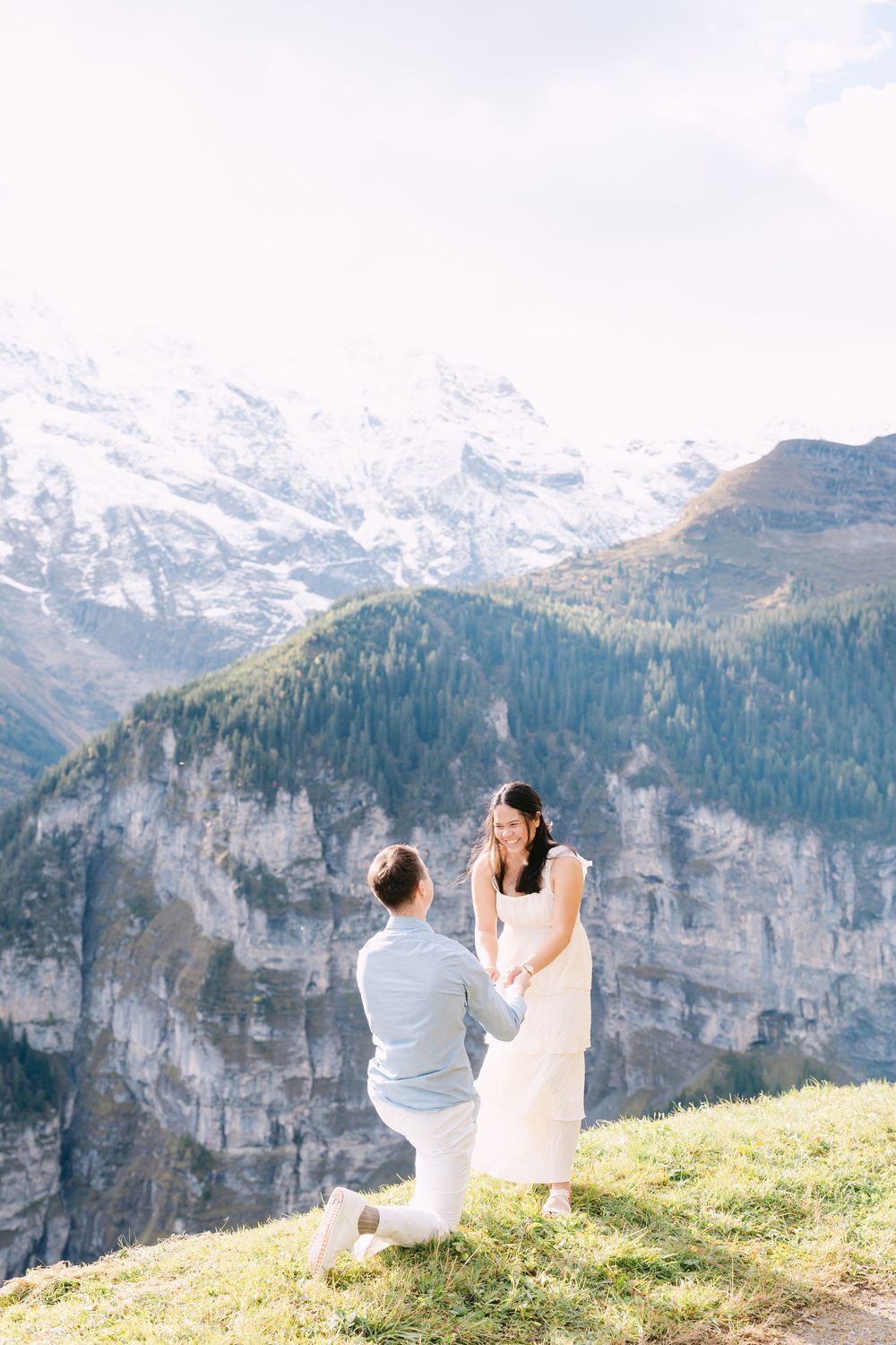 A romantic proposal moment on a mountain cliff overlooking snow-capped Swiss Alps and lush green valleys in Mürren.