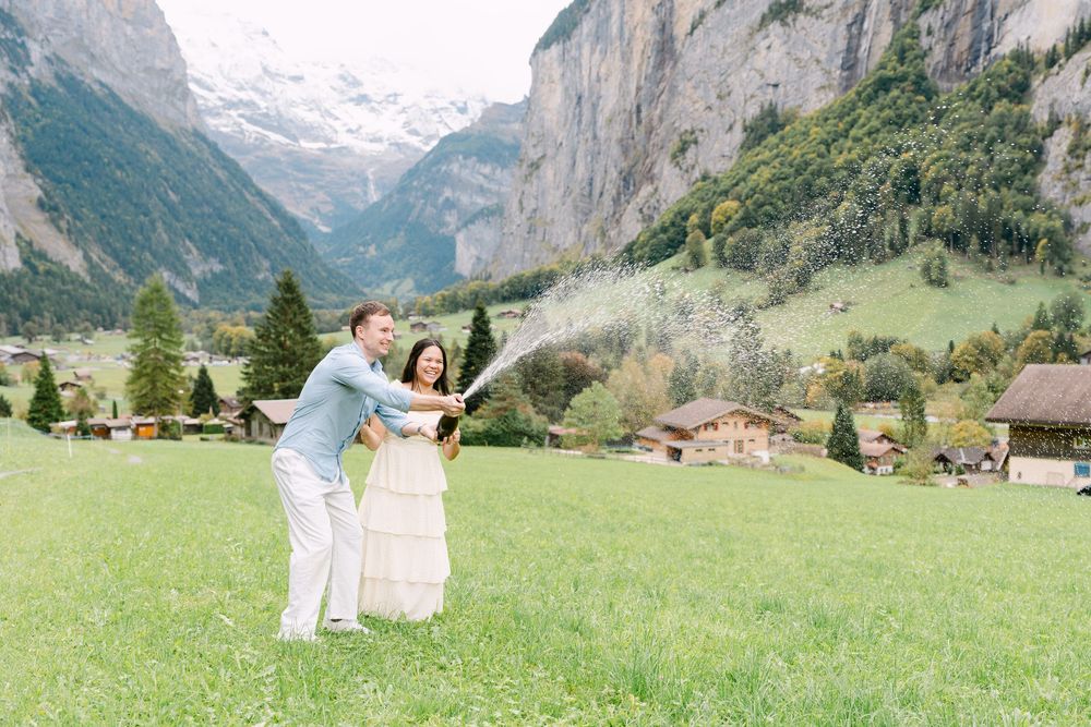 Two people in white outfits dance joyfully in a lush green meadow in Lauterbrunnen with majestic Swiss Alps mountains in the background.