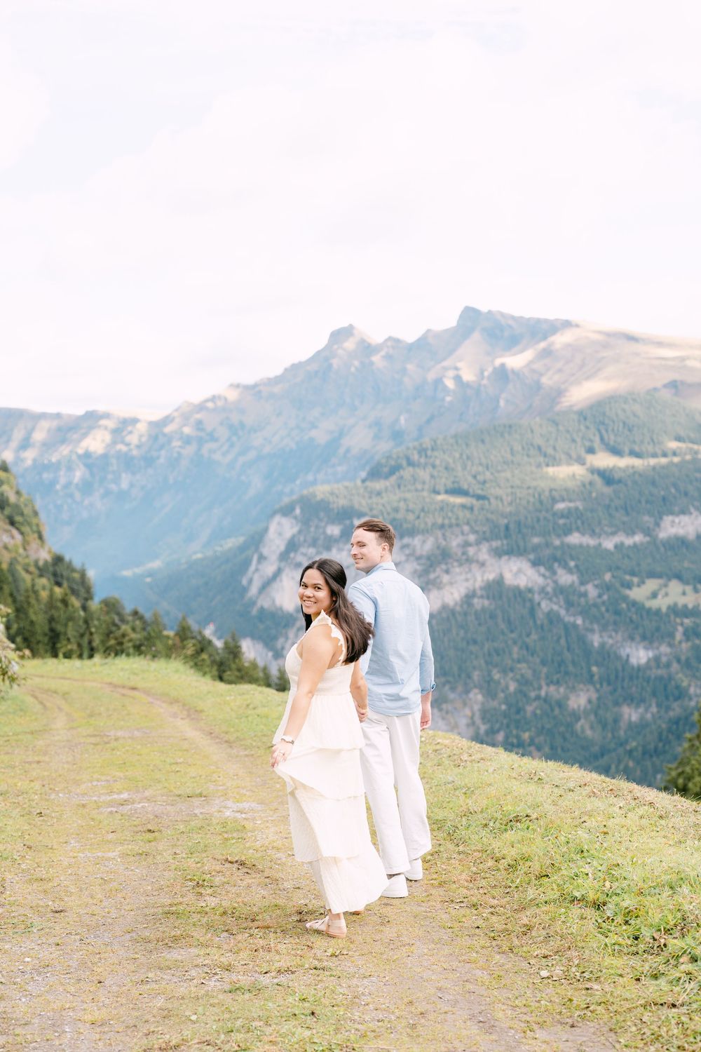 A couple stands together on a mountain trail overlooking majestic snow-capped peaks in the distance in Mürren.