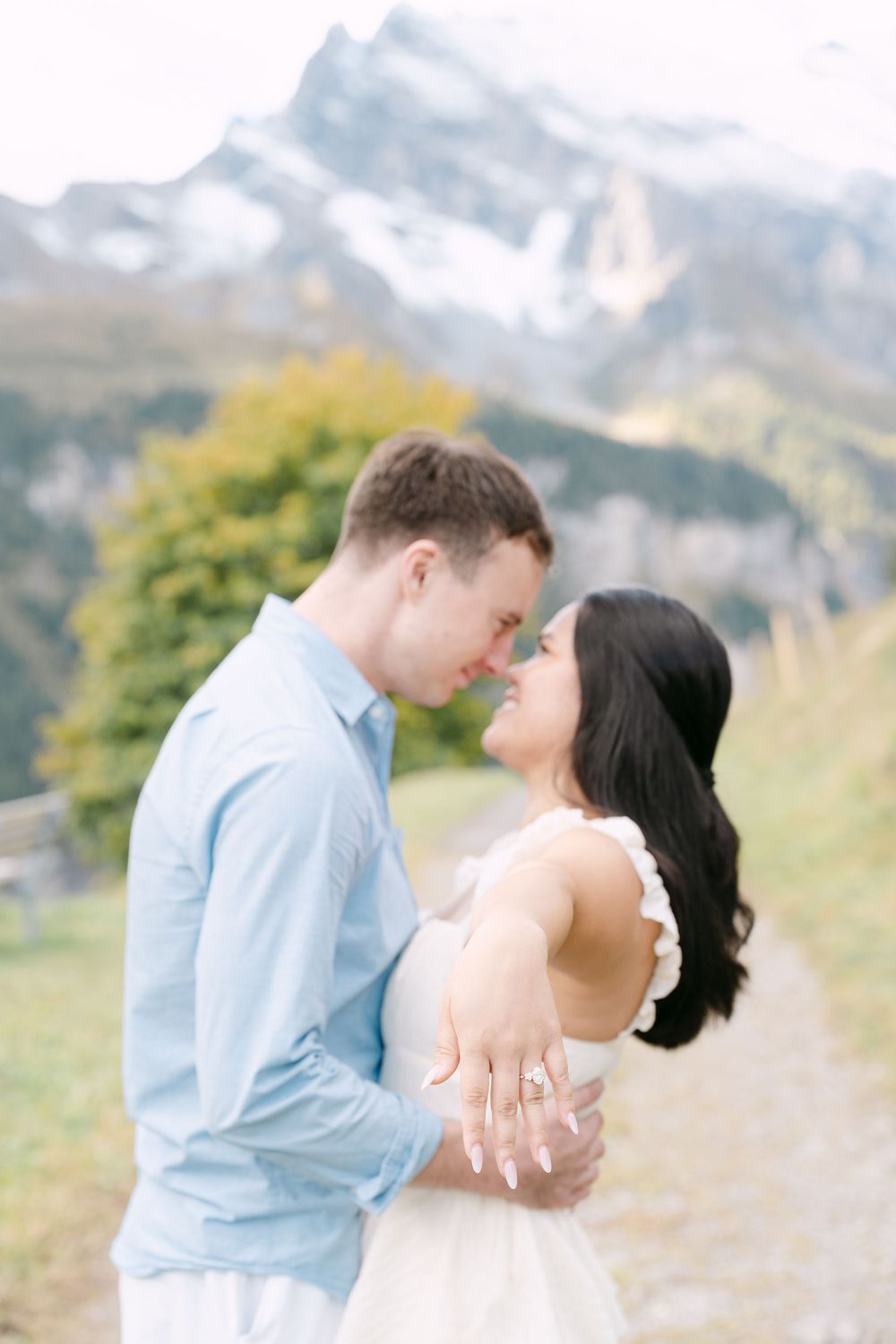 A couple shares an intimate moment in a mountain meadow with snow-capped peaks in the background.