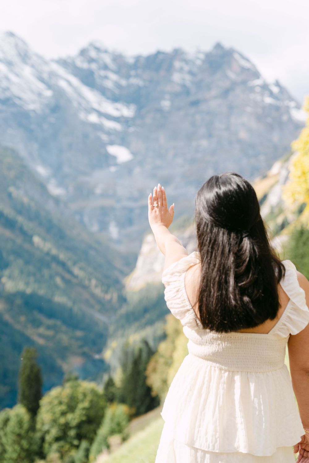 Person in white dress raises hand towards majestic snow-capped mountains in Swiss Alps landscape in Mürren.