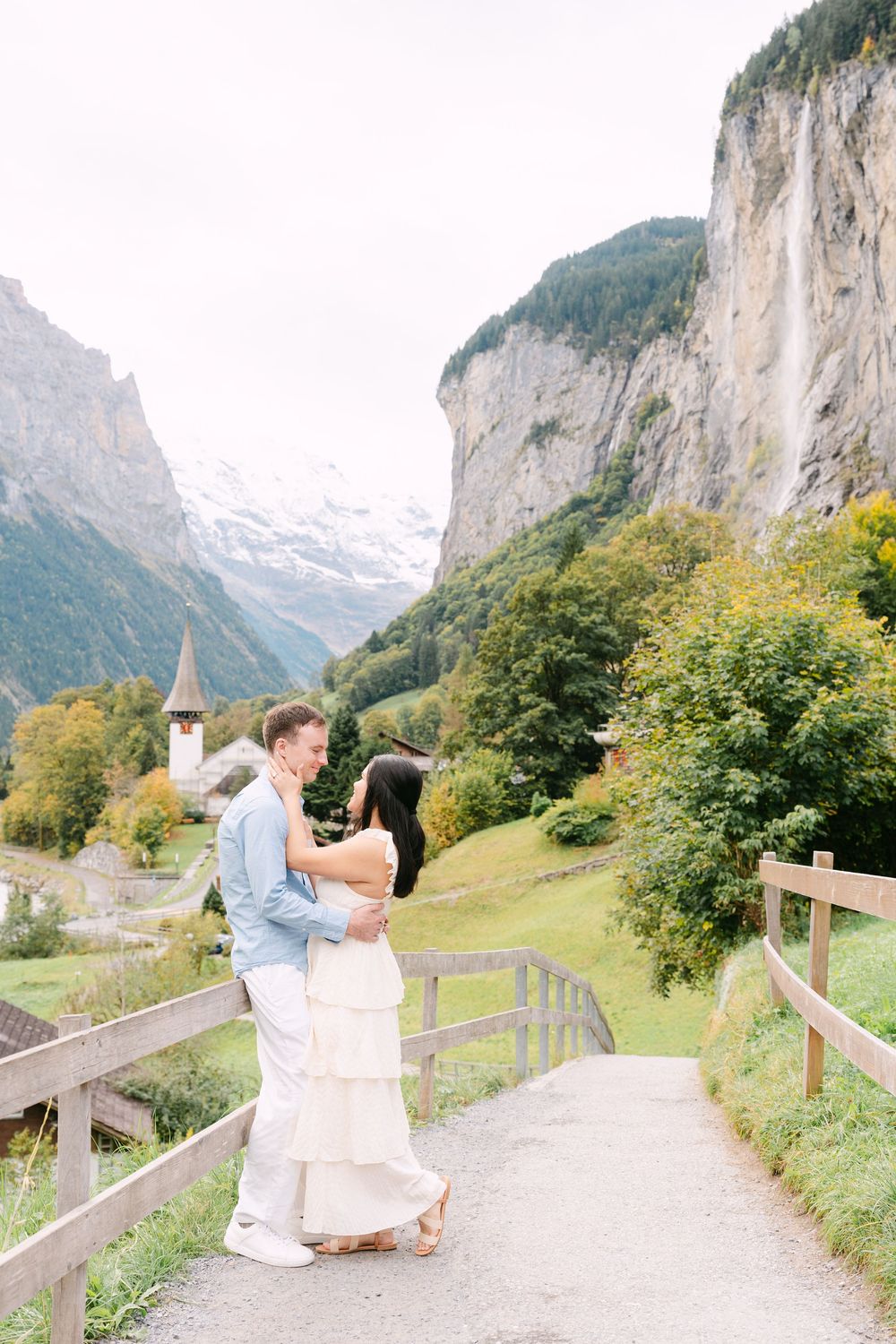 A romantic moment captured on a rustic mountain path with towering Alpine cliffs and the famous Staubbachfall waterfall in Lauterbrunnen.