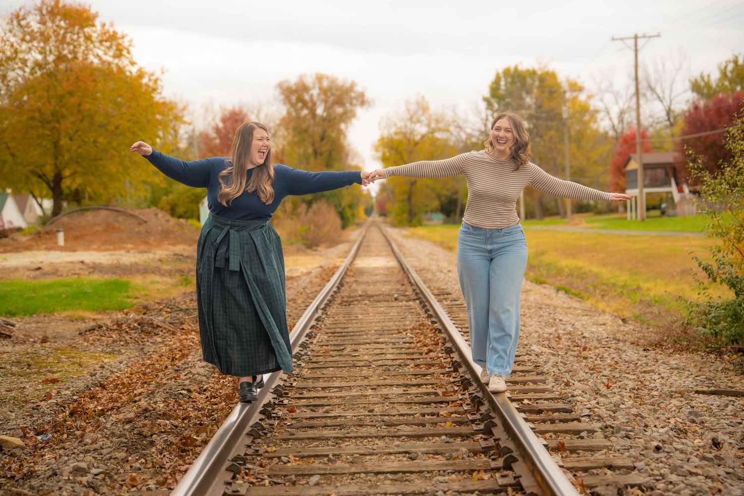 Two sisters walk hand in hand along rustic train tracks surrounded by autumn foliage at sunset. Quad Cities Family Photography.