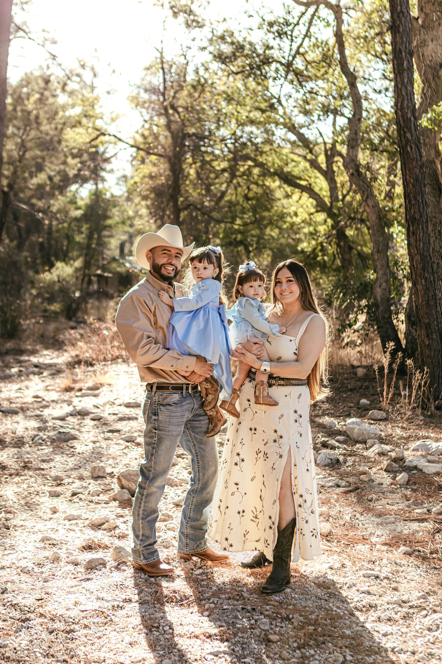 Family photoshoot in a sunlit forest setting with natural earth tones.