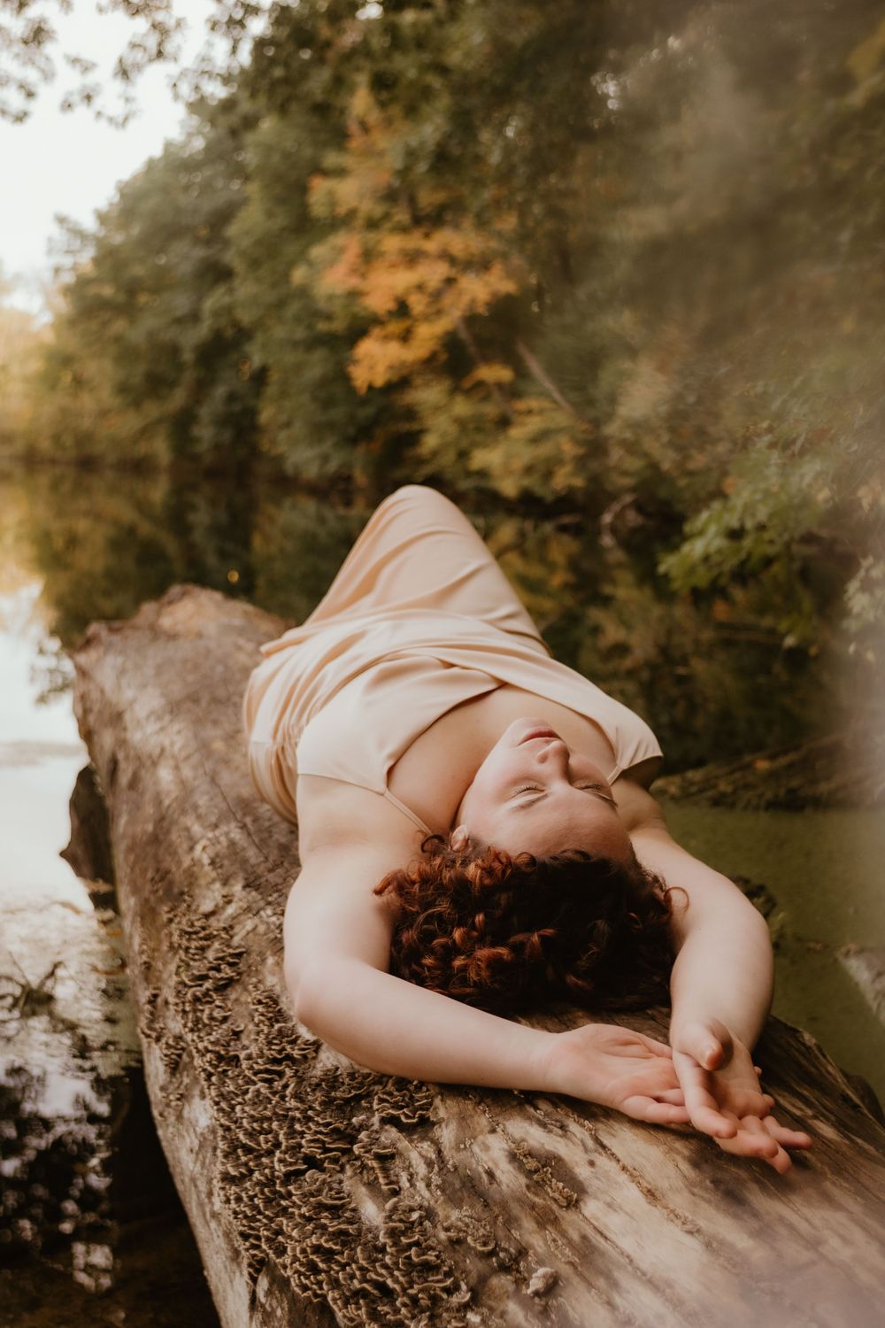 A dreamy portrait series shows a person in flowy fabric reclining on rocks beside a reflective pond in autumn light.