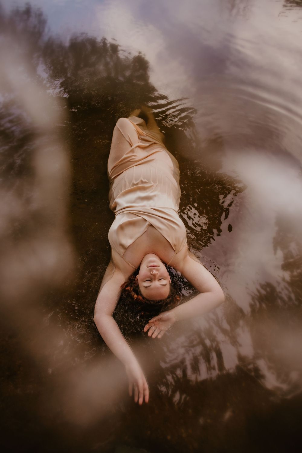 A dreamy ethereal portrait of a figure floating in dark water with soft moody lighting and reflections.